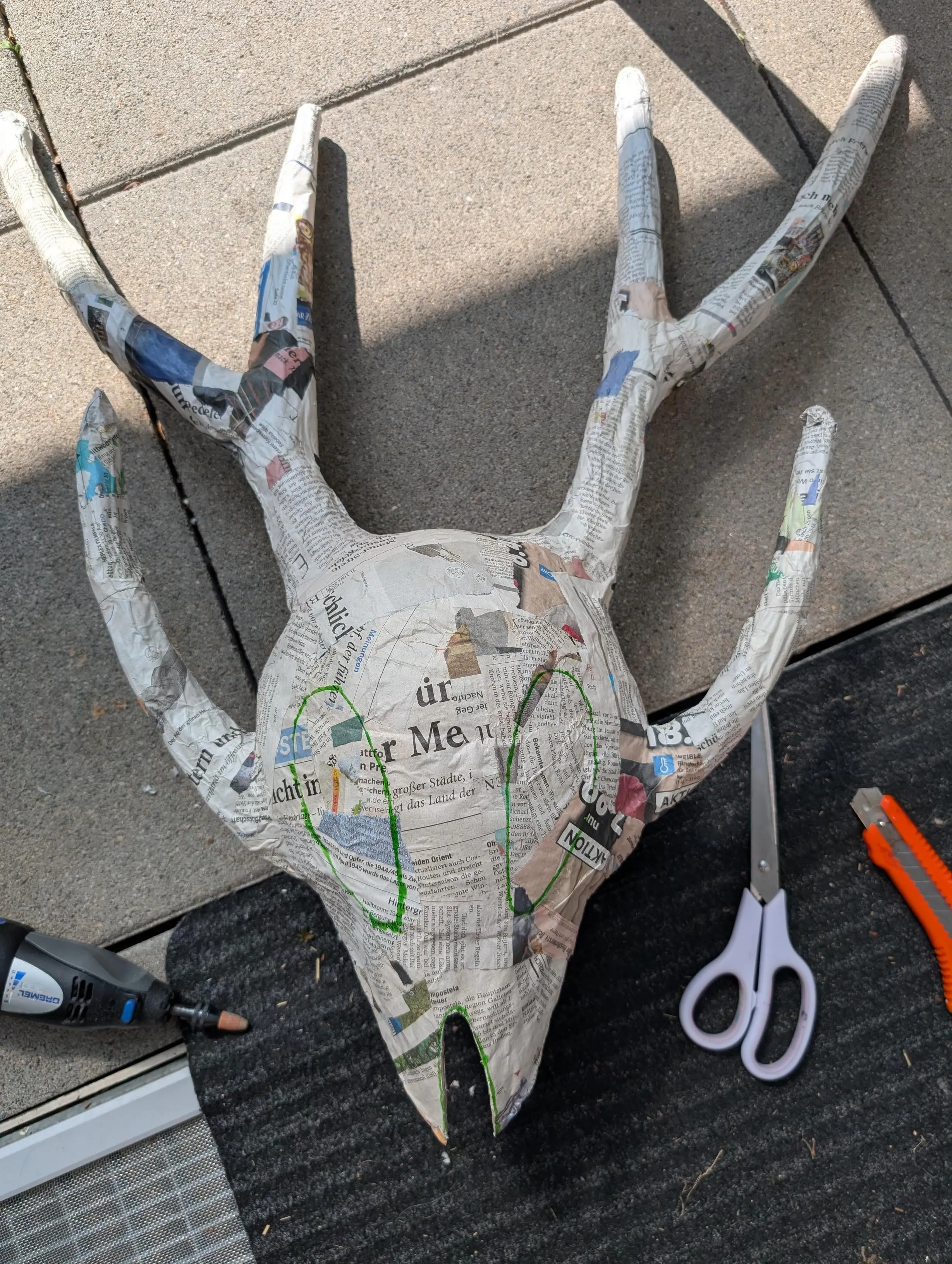 The mask made of paper mache laying on the ground outside, with eye holes drawn on to be cut.